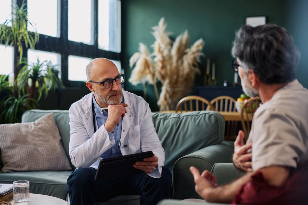 Doctor conducting a calm home consultation with an older male patient on a comfortable living room sofa